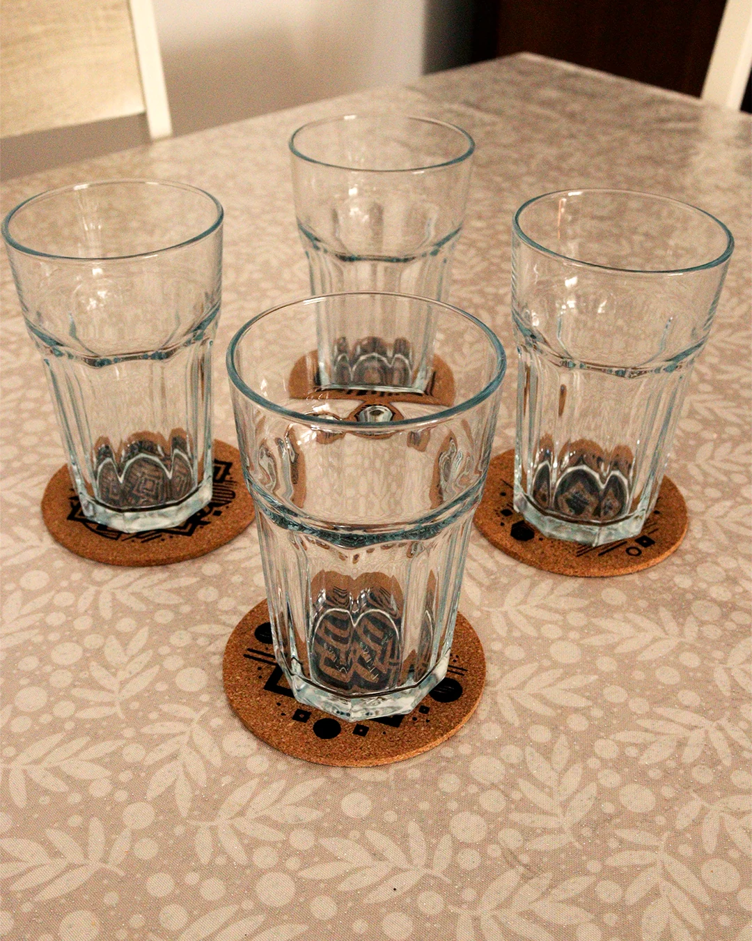 Bases de copos em cortiça com formas geométricas sobre a mesa com copos.